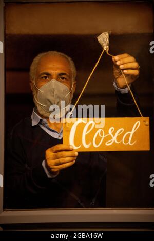 UN UOMO ANZIANO CHE INDOSSA UNA MASCHERA CHE APPENDE LA LAVAGNA A CARTELLI CHIUSI Foto Stock