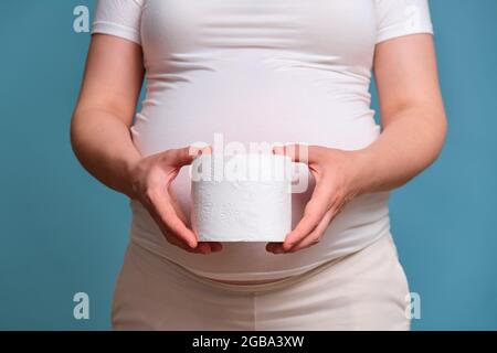 Carta igienica in mani di donna incinta, studio girato su sfondo blu Foto Stock