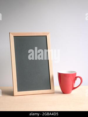 Lavagna vuota con tazza di caffè rossa su tavolo di legno. Sfondo grigio bianco. Foto Stock