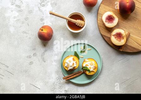 Pesche cotte su un piatto con foglie di menta, cannella, formaggio cremoso non caseario, miele e fiocchi di mandorle. Foto Stock