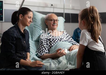 Anziano ammalato anziano anziano che riposa a letto parlando con la nipote che si prende cura dopo il reparto ospedaliero di perizia medica. Nonno godendo di passare il tempo con il bambino durante la chirurgia clinica. Trattamento sanitario Foto Stock