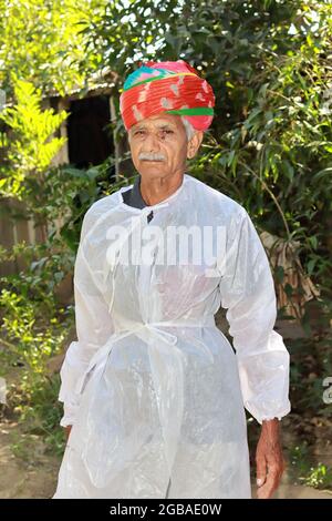 Un contadino asiatico in posa in un giardino con un turbano tradizionale colorato e vestito bianco con sfondo di giardino sfocato Foto Stock