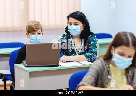 Bambini e insegnanti con maschera di protezione di ritorno a scuola in classe dopo il covid-19 blocco Foto Stock