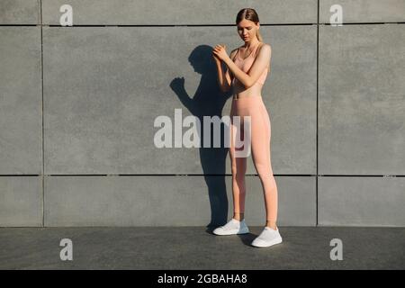 Vista laterale scatto di giovane donna in forma che fa squats, l'esercizio sulle natiche all'aperto, l'allenamento sulla parete di cemento urbano sfondo, fitness femminile esercizio outd Foto Stock