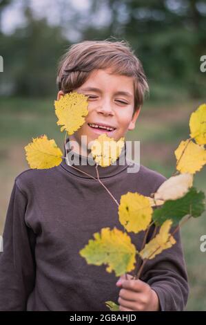 Ragazzo felice con una luce di foglie gialle Foto Stock