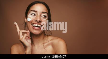 Donna sorridente che applica la maschera facciale. Primo piano di una giovane donna che applica il prodotto per la pelle. Foto Stock