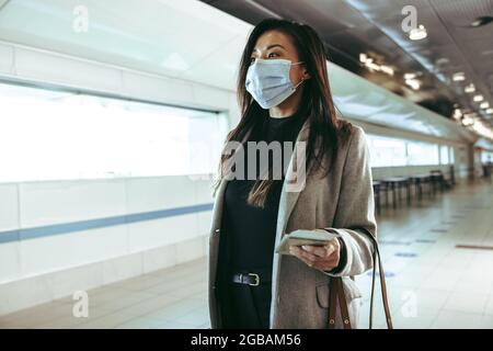 Uomo d'affari che indossa maschera protettiva per il viso in viaggio in aria. Una donna che cammina attraverso il corridoio vuoto dell'aeroporto durante la pandemia. Foto Stock