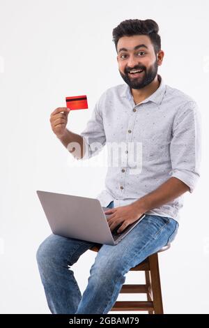 UN UOMO FELICE BEARDED CHE MOSTRA LA CARTA DI DEBITO DAVANTI ALLA MACCHINA FOTOGRAFICA Foto Stock