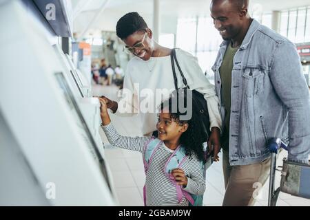 Piccola ragazza felice di usare la macchina self-service per il check-in all'aeroporto con i suoi genitori. Famiglia di tre persone presso l'aeroporto internazionale di check-in automatico macchina Foto Stock