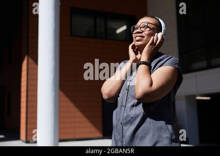Donna africana in cuffie wireless che ascolta la musica mentre ti trovi all'aperto Foto Stock