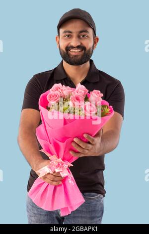 UN FELICE UOMO DI CONSEGNA BEARDED IN PIEDI E CHE TIENE BOUQUET DI FIORI Foto Stock