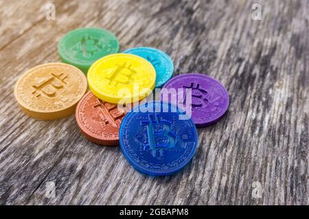 Monete di Bitcoin in colori arcobaleno su sfondo di legno. Valuta criptata artigianale multicolore. Sette monete diverse in rosso, arancione, giallo, verde, Foto Stock