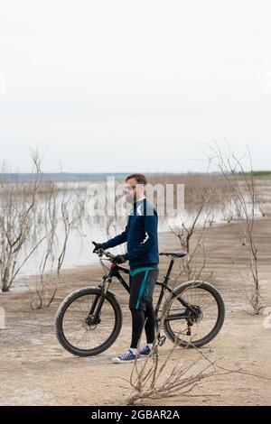 Ciclista su una mountain bike su una spiaggia di sale sullo sfondo di canne e un lago Foto Stock