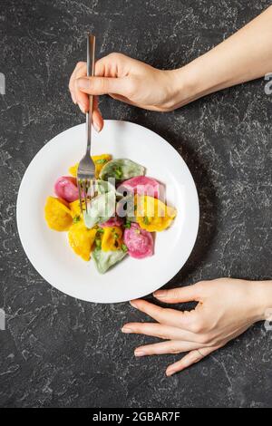 Gnocchi multicolore di pasta colorata ripiena di carne su fondo di pietra nera. Forcella per maniglie femmina. Vista dall'alto Foto Stock