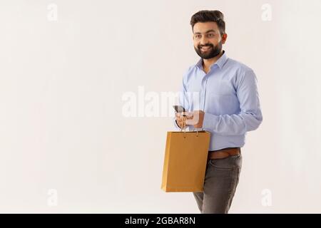 UN UOMO INTELLIGENTE CHE CAMMINA MENTRE TIENE IL TELEFONO CELLULARE E LA BORSA DI CARTA Foto Stock