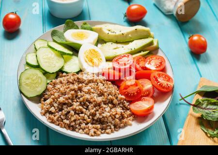 Ciotola da pranzo vegana con avocado, uovo, cetriolo, pomodoro e grano saraceno su sfondo di legno Foto Stock