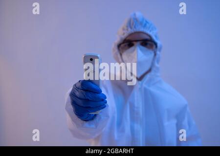 Un operatore sanitario in kit DPI con una pistola per il controllo della temperatura. Foto Stock
