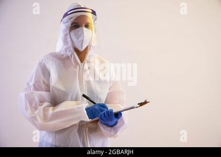 Un operatore sanitario in kit PPE che contiene un blocco note e una penna. Foto Stock