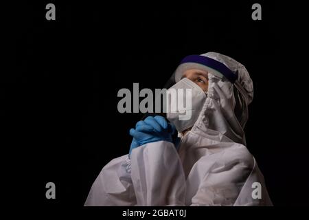 Un medico in kit PPE si unisce alle mani in preghiera. Foto Stock