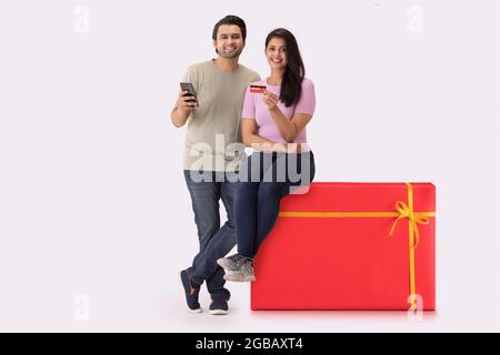 Una giovane donna seduta su uno sgabello a forma di regalo con un uomo accanto, mostrando carta di credito e telefono. Foto Stock