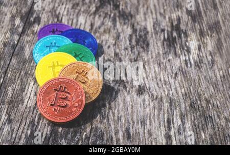 Monete di Bitcoin in colori arcobaleno su sfondo di legno stagionato con spazio copia. Valuta criptata artigianale multicolore. Sette monete diverse in re Foto Stock