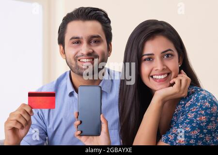 Un giovane uomo e una donna seduti in camera con carta di credito e telefono cellulare. Foto Stock