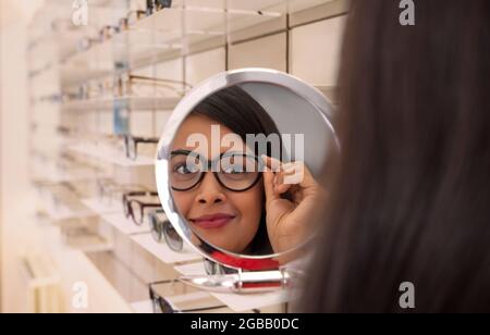 Una giovane donna che prova lo spettacolo incornicia nello specchio presso un negozio di ottico. Foto Stock