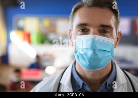 Ritratto di un medico caucasico che indossa una maschera facciale nella classe a scuola Foto Stock