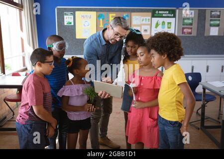 Insegnante di sesso maschile caucasico con gruppo di insegnamento di tavolette digitali di diversi studenti in classe ambiente Foto Stock