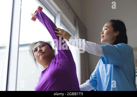 Fisioterapista femminile asiatica che cura la paziente femminile asiatica a casa sua Foto Stock