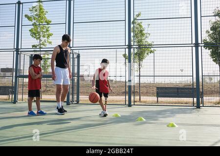 Allenatore di basket che insegna a due bambini come giocare, uno ha una protesi. Foto Stock