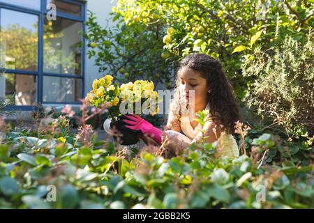 Sorridente ragazza mista di razza piantando fiori in cortile Foto Stock