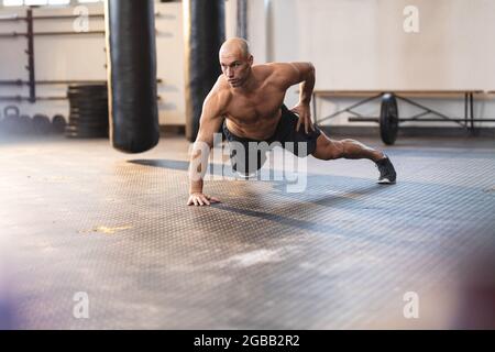 Forte uomo caucasico che si esercita in palestra, facendo push-up con una mano Foto Stock