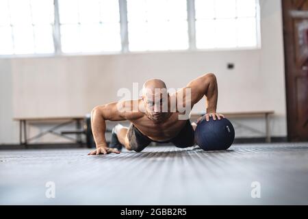 Forte uomo caucasico che si esercita in palestra, facendo push-up utilizzando la palla Foto Stock