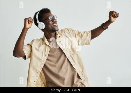 Giovane africano con cuffie wireless che ascolta musica e balla su sfondo bianco Foto Stock