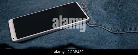 telefono cellulare bianco panorama su jeans blu Foto Stock