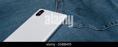 telefono cellulare bianco panorama su jeans blu Foto Stock
