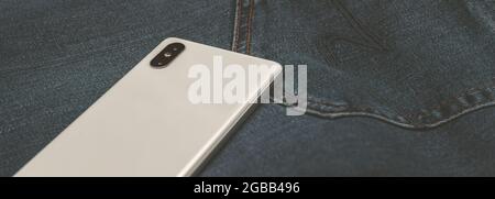 telefono cellulare bianco panorama su jeans blu Foto Stock