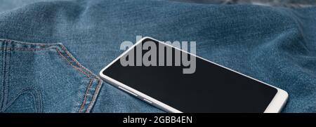 telefono cellulare bianco panorama su jeans blu Foto Stock