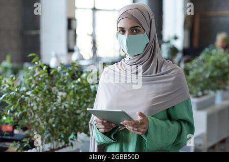 Giovane uomo d'affari musulmano in hijab e maschera protettiva guardando la macchina fotografica Foto Stock
