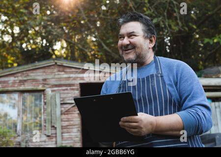 Ritratto di sorridente giardiniere maschio caucasico usando una tavoletta al centro del giardino Foto Stock