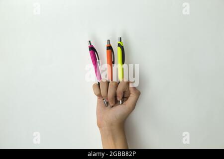 mano di una ragazza che tiene tre penne di un colore diverso tra le dita su sfondo bianco Foto Stock