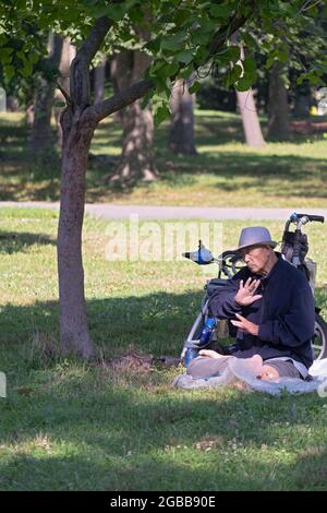 Un uomo seduto di 86 anni fa Falun Gong slow-moving esercizi vicino ad un albero. In un parco a Queens, New York, un luogo molto diverso. Foto Stock