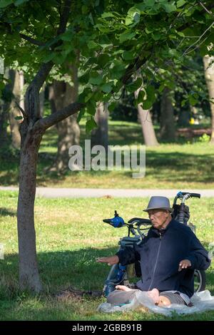 Un uomo seduto di 86 anni fa Falun Gong slow-moving esercizi vicino ad un albero. In un parco a Queens, New York, un luogo molto diverso. Foto Stock