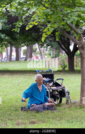 Un uomo seduto di 86 anni fa Falun Gong slow-moving esercizi vicino ad un albero. In un parco a Queens, New York, un luogo molto diverso. Foto Stock