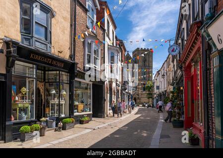 Vista di negozi e caffè su Kirkgate e Cattedrale sullo sfondo, Ripon, North Yorkshire, Inghilterra, Regno Unito, Europa Foto Stock