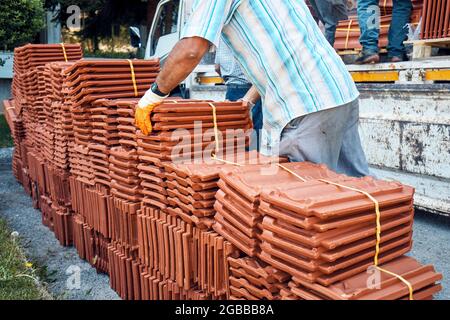 Addetto alla costruzione che dispone lotti di tegole del tetto scaricati da un camion. Foto Stock