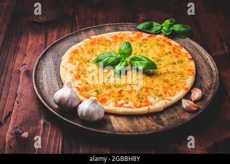 Pane per pizza con aglio, formaggio e basilico su sfondo ligneo Foto Stock