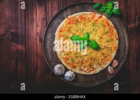 Pane per pizza con aglio, formaggio e basilico su sfondo ligneo Foto Stock