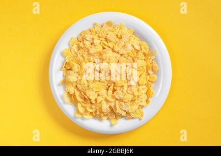 Cornflakes in piastra bianca su sfondo giallo, vista dall'alto Foto Stock